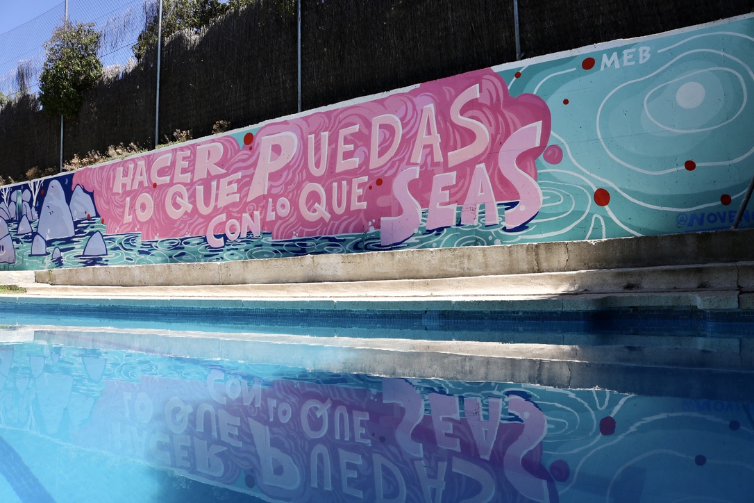 Pintura mural en un muro donde pone "Hacer lo que seas con lo que puedas" al lado de una piscina